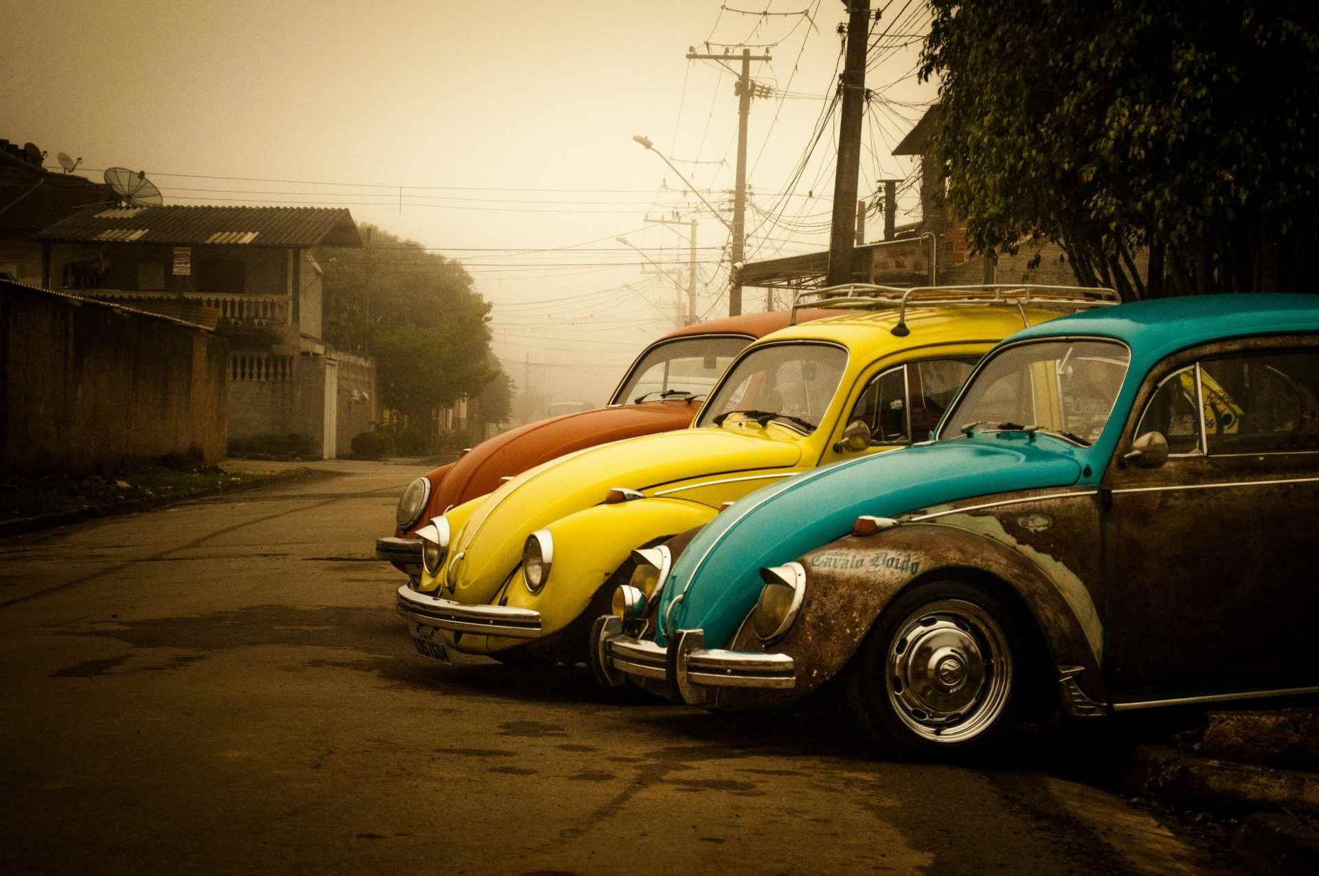 drei verschiedene Farben Volkswagen Käfer Coupés in der Nähe von Häusern geparkt